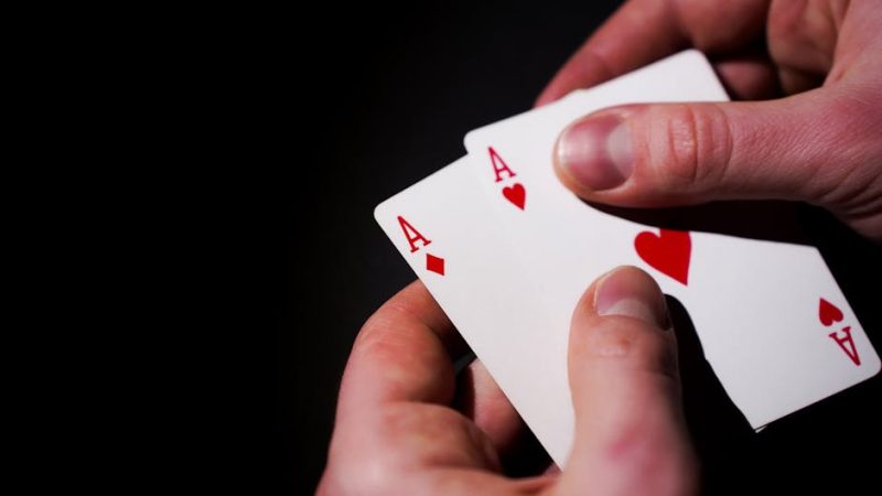 Hands holding three aces against a dark background, symbolizing luck and skill in card games.