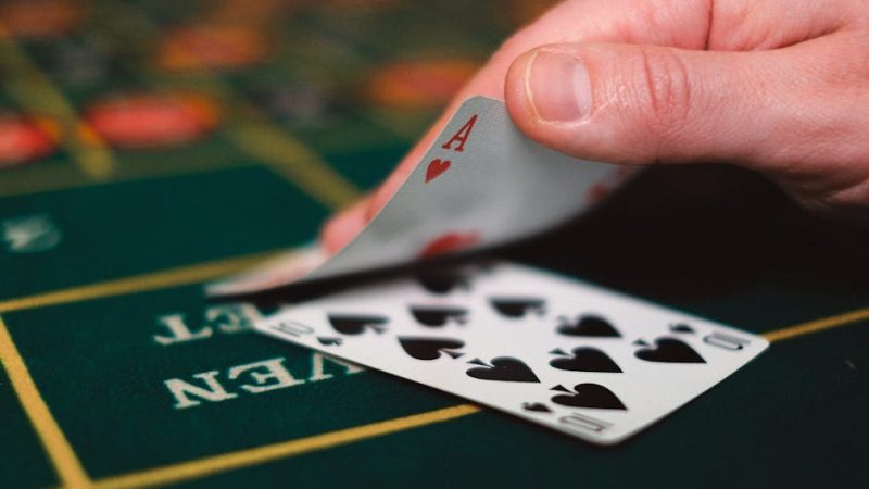 Close view of playing cards and hand on a casino table, capturing the gambling atmosphere.