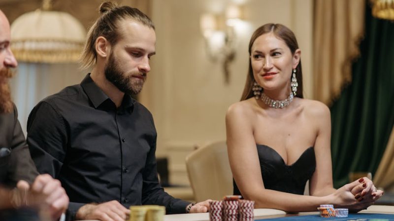 Man and woman sitting together at a casino gaming table with poker chips, exuding elegance and leisure.