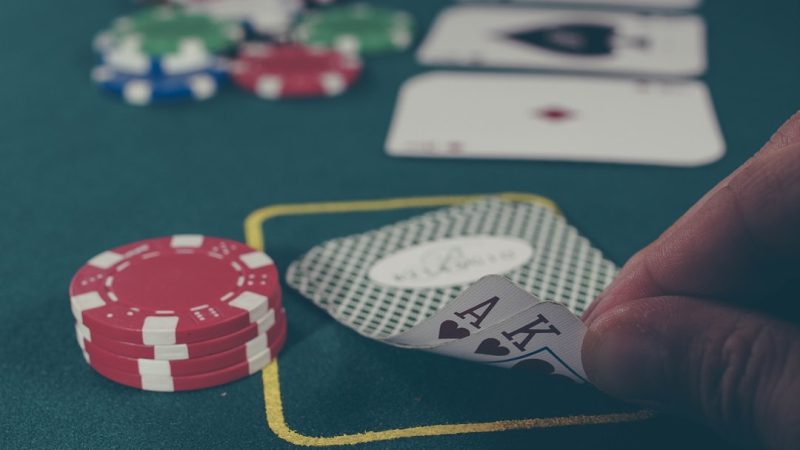 person holding black ace and king spades playing cards on poker table